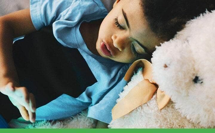 A child reading his tablet in bed with his teddy bear